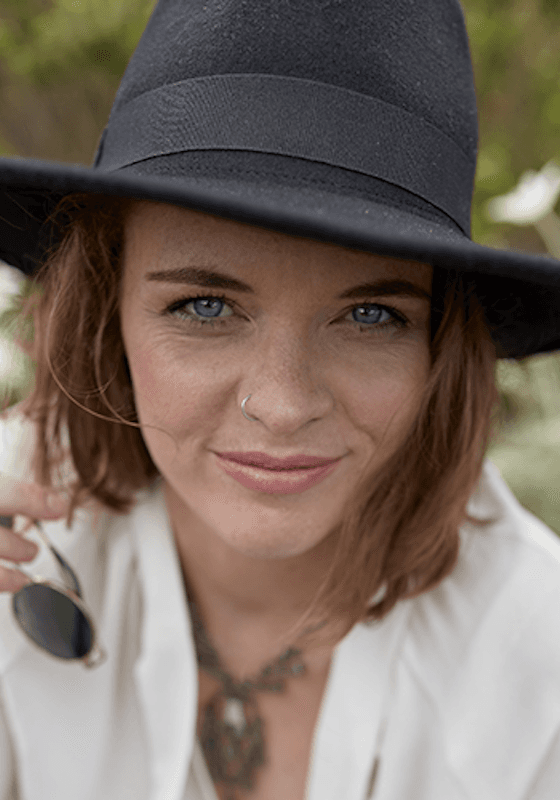 Headshot of Tabatha Lionheart, they look relaxed, wearing a black hat and has brown hair.