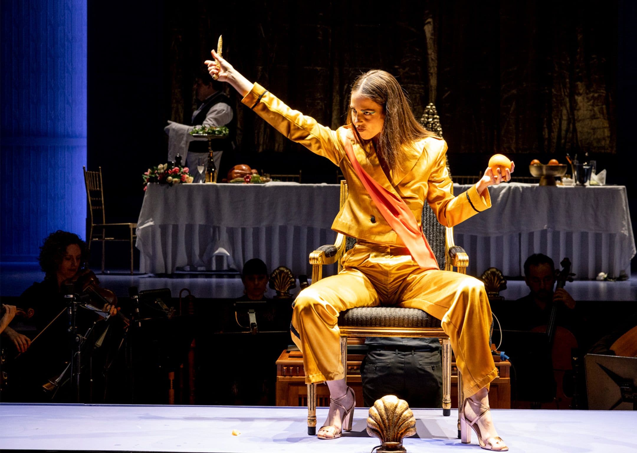 Orontea production still by Brett Boardman of Anna Dowsley wearing a gold suit, seated in a gold chair performing onstage at City Recital Hall