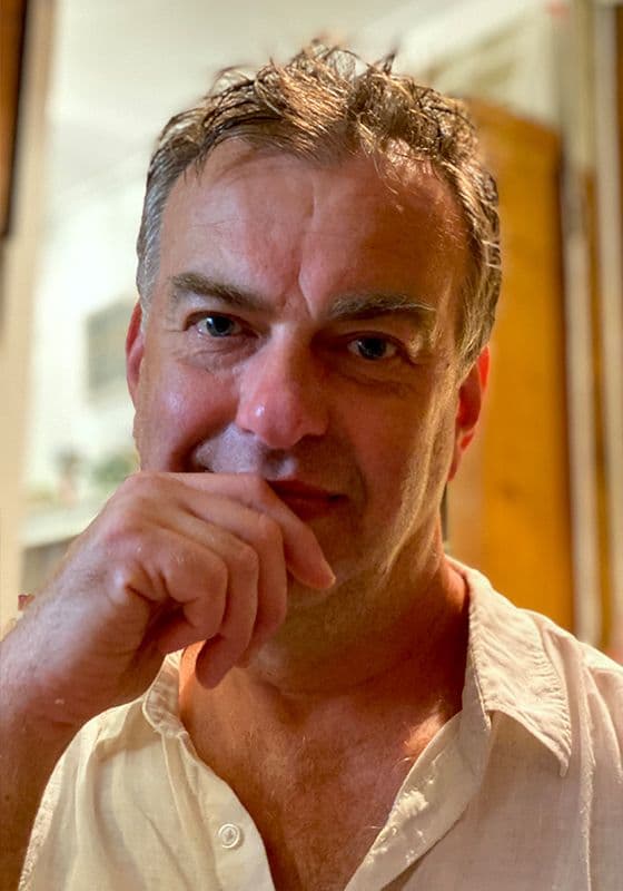 Headshot of Andrew Johnston, relaxed with hand resting on chin, with short dark hair