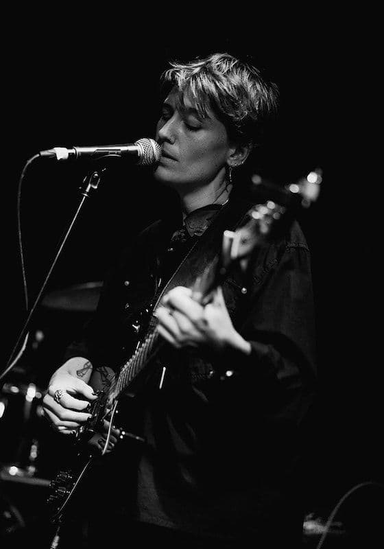 Headshot of Gabriela Ellicott, singing into a microphone while playing a guitar